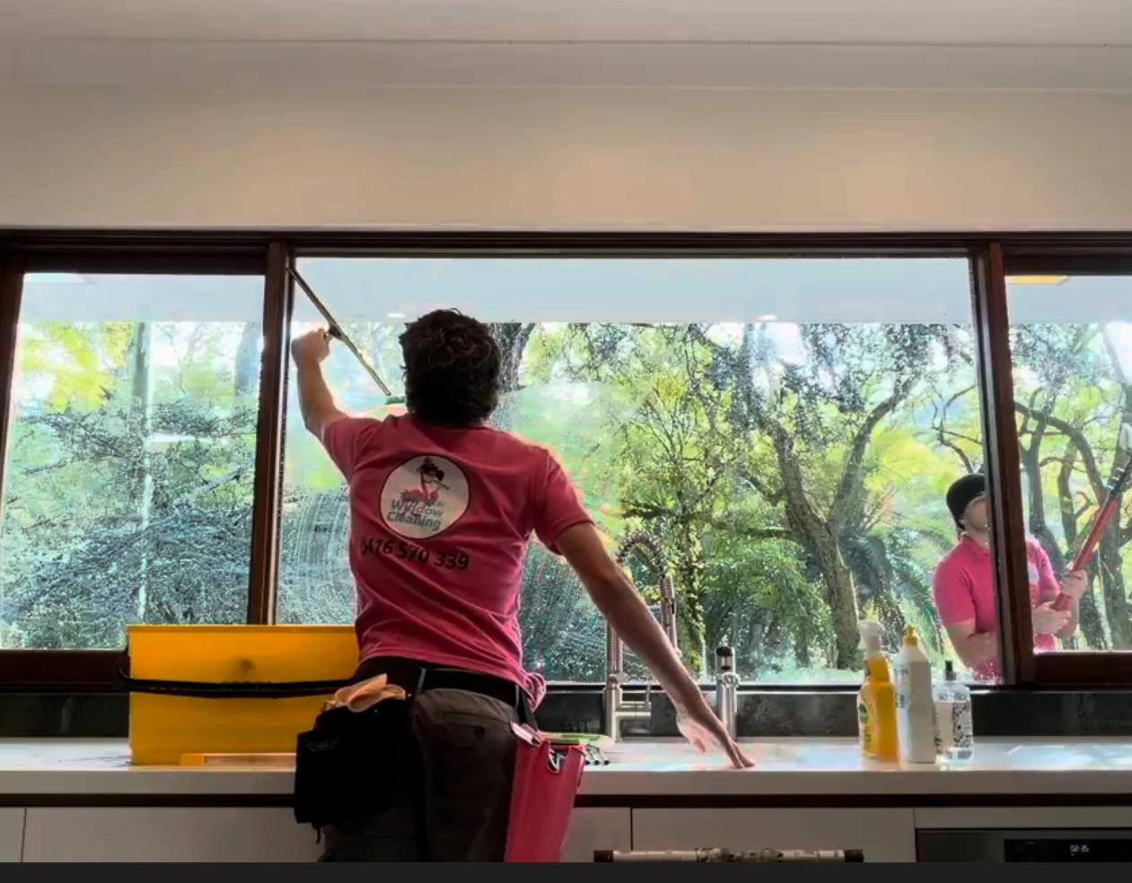 Flamingo Window Cleaning technician in a pink uniform squeegeeing a large kitchen window